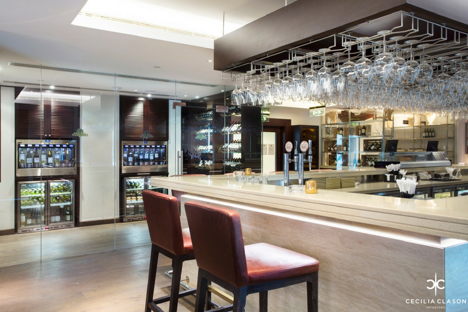 Bar Interior Design - White granite bar counter top with dark wood overbar glass rack, leather bar stools & glass wine cellar