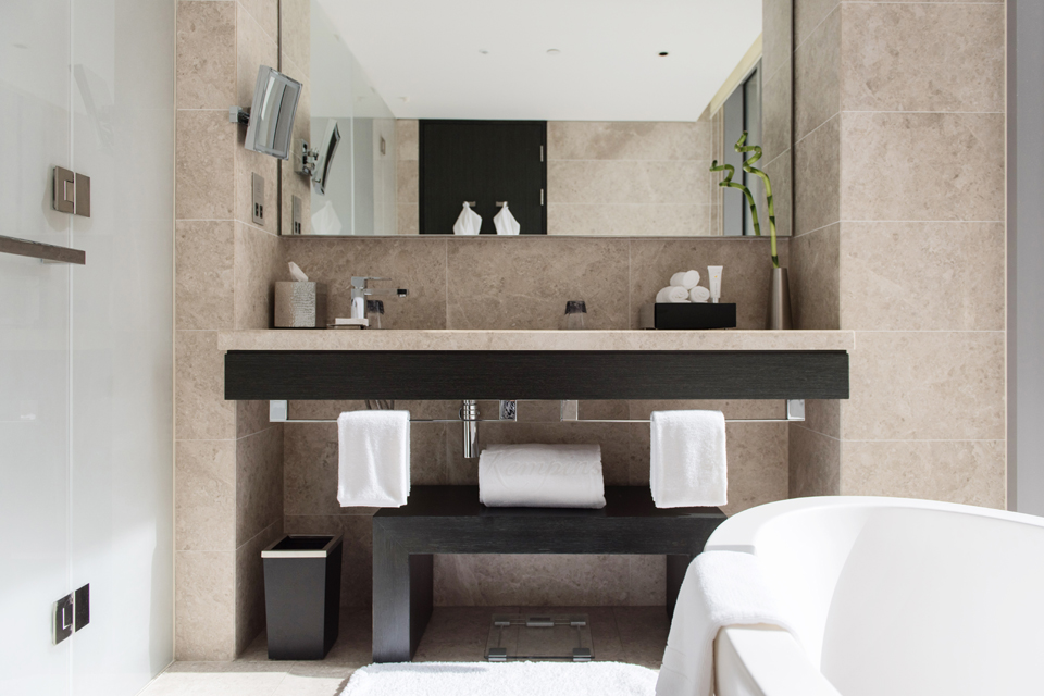Bathroom Interior Design - Textured, tiled walls & countertop with dark, solid wood furniture next to frosted glass door