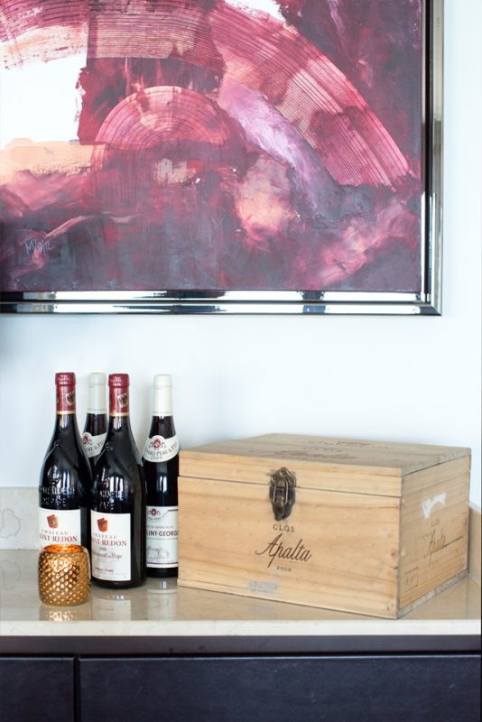 Office Interiors - Abstract wall art with gold candle holder next to wine and wooden wine box on granite counter top