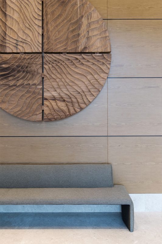 Lobby Interior Design - Large circular wooden wall art feature against wood paneled wall with modern seating