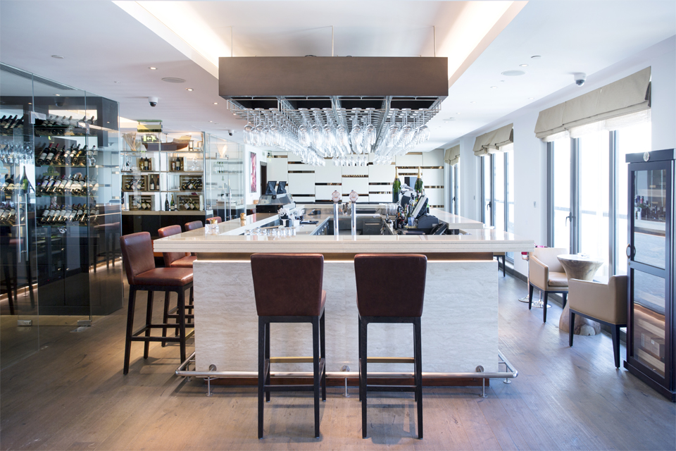 Bar Interior Design - White granite bar counter top with dark wood overbar glass rack, leather bar stools & glass wine cellar
