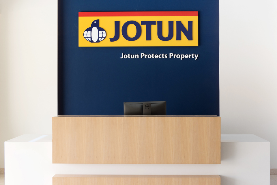 Commercial Office Reception Design - White desk with wooden partition and Jotun logo on dark blue wall