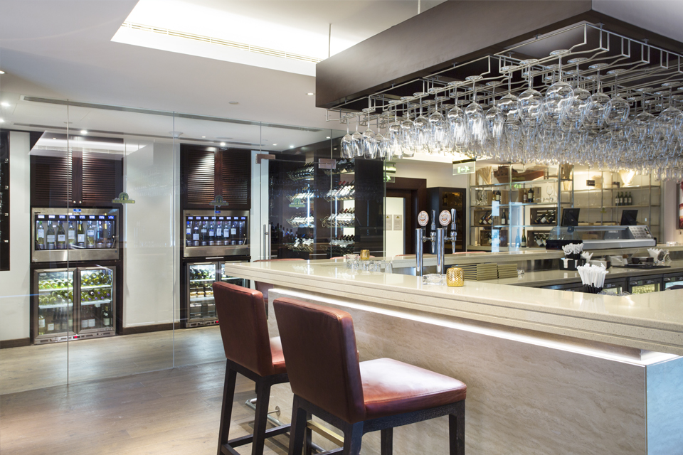Bar Interior Design - White granite bar counter top with dark wood overbar glass rack, leather bar stools & glass wine cellar